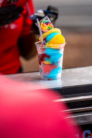 Colorful swirled ice cream dessert in clear plastic cup with vibrant blue and red hues.