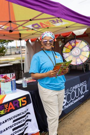 Arts Council booth setup with purple banners and staff in blue shirts at outdoor event.