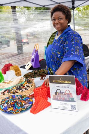 A vendor displays colorful handmade items and books at an outdoor market table.
