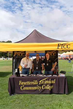 College recruitment booth with yellow banner and staff members at an outdoor community event.