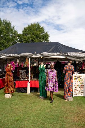 Colorful dresses and clothing displayed on racks at an outdoor market under black pop-up tents on grass.