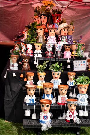 Clay pot people crafts with painted faces and outfits displayed under a red tent at an artisan market.