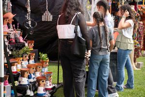 A crowd of people standing in line at an outdoor market or festival with vendor booths visible in the background.