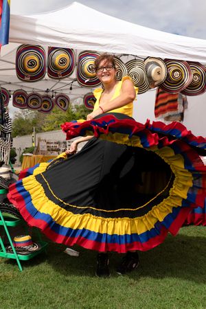 Vibrant traditional dresses with black, red, yellow and blue ruffles displayed under a white tent.