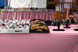 Merchandise display table with t-shirts and jewelry laid out on a pink tablecloth at a vendor event.