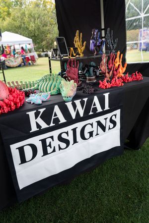 Black vendor table with 'Kawai Designs' text display at an outdoor craft market.