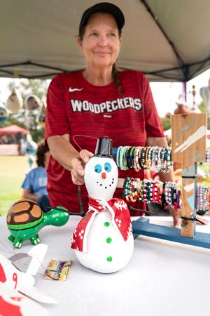 Ceramic snowman decorations and holiday crafts displayed on a white table at an outdoor market.