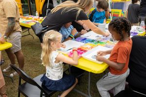 Young children engage in colorful art activities at outdoor yellow tables.