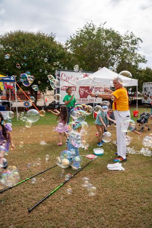 Children play with bubbles on a grassy field at an outdoor festival or event.