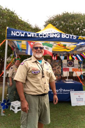 Boy Scout representatives in uniform standing near recruitment banner at community event.