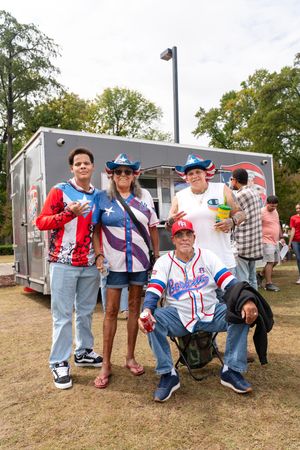 Group wearing patriotic attire poses near a trailer at an outdoor event.