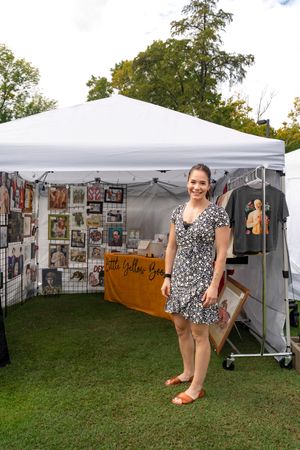 White vendor tent displaying artwork and photographs at an outdoor festival.