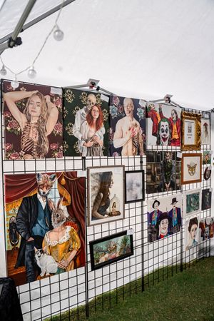 Art gallery display featuring multiple colorful paintings mounted on white grid panels outdoors.