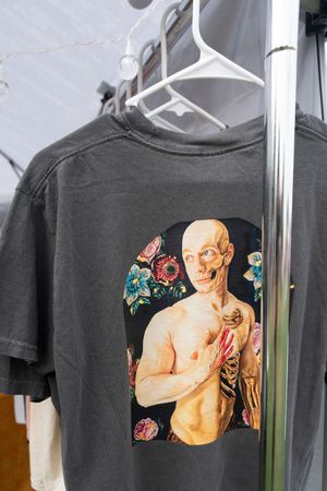 Black t-shirts with renaissance art prints displayed on hangers at a market stall.