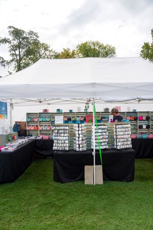 White canopy tent displaying rows of merchandise on black-draped tables at an outdoor market.
