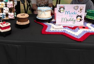 Display of decorated cakes and baked goods on black tablecloth at market stall.