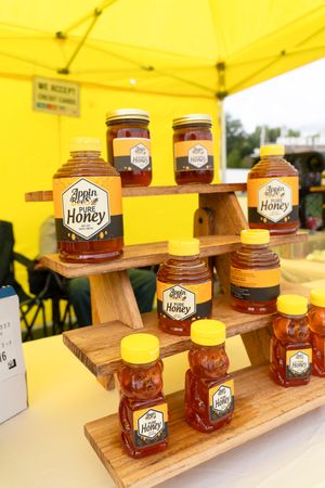 Wooden display shelves stocked with glass jars of golden honey under a bright yellow canopy.