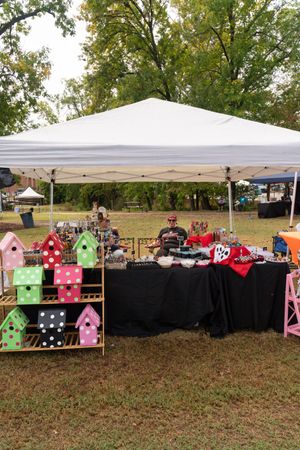 Outdoor market stalls with colorful birdhouses and merchandise displays under white canopy tents.