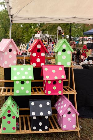Colorful polka dot birdhouses displayed on wooden shelves at a craft fair vendor booth.