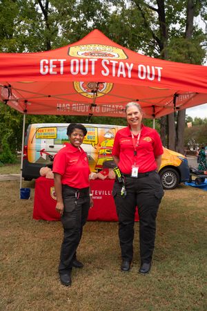 Staff members in red uniforms stand in front of a safety awareness booth at a community event.
