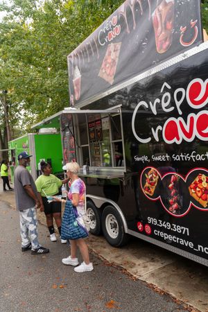 Black food truck with 'Crepe' branding serving customers at an outdoor event.