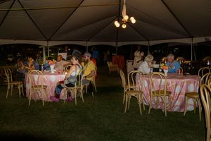 Outdoor evening event setup with white tents and tables decorated with pink tablecloths under dim lighting.