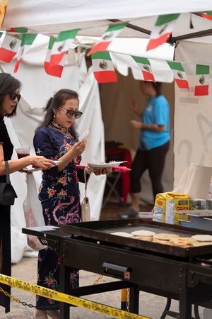 Food vendors cooking at outdoor festival with Mexican flags hanging overhead.