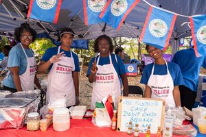 Food vendor booth with Belize flags displaying homemade dishes and treats at a cultural festival.