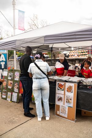 Row of vendor tents with display boards showing food menu items at an outdoor market.