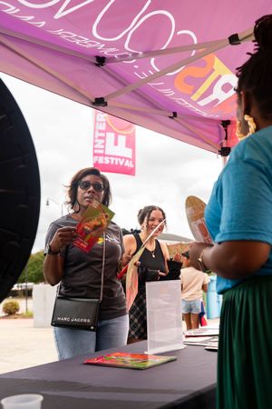 Festival attendees interact with vendors at a booth under a pink tent during an outdoor event.