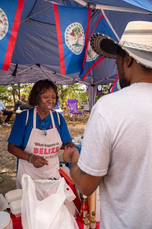 Vendors prepare and serve Belizean food under a blue tent at an outdoor festival or market. Photography by Tim Ellis