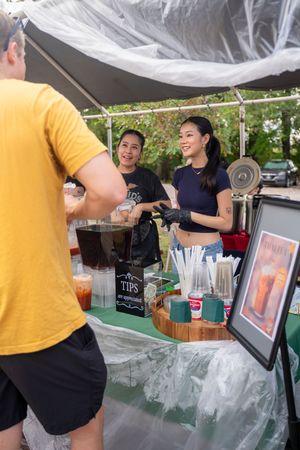 Beverage service station with ice bins and drink dispensers set up under outdoor tent.