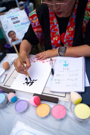 Colorful face painting supplies and drawing materials laid out on table with hands working on designs.