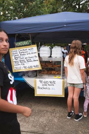 Food vendor stalls with handwritten menu signs for Honduran cuisine at outdoor market.