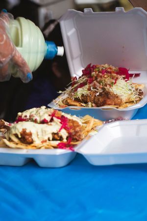 Row of loaded nachos plates with toppings and sauces served on a blue tablecloth.