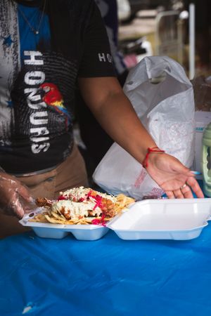 Food being served on white paper plates at an outdoor event with blue tablecloth.