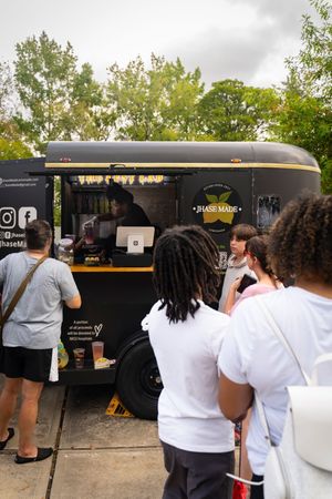 People waiting in line at black food trucks on a cloudy day at an outdoor event.