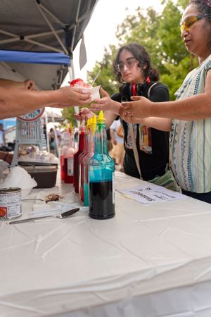 Bottles of colorful syrup arranged on white tablecloth at outdoor vendor booth.