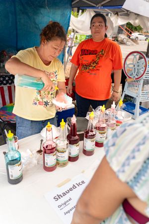 Vendors serving colorful drinks and beverages at an outdoor market stall.