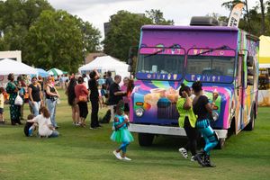 Colorful ice cream truck surrounded by festival attendees on a grassy field.