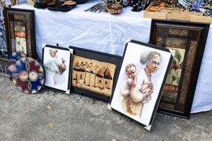Row of framed artwork and photographs displayed on the ground against a wall.