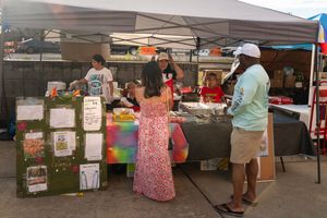 Outdoor market stalls with white canopy tents and vendors set up in a row.