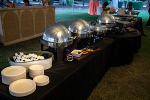 Elegant catering setup with multiple chafing dishes and buffet warmers arranged on black tablecloths at an event.