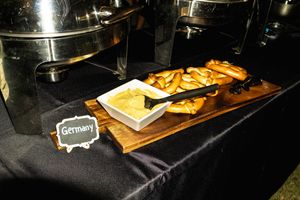 Wooden serving board with appetizers and snacks displayed next to catering equipment on a black tablecloth.