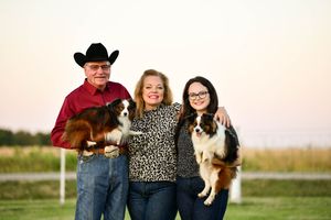 Family group posing outdoors with their pet dogs during sunset.