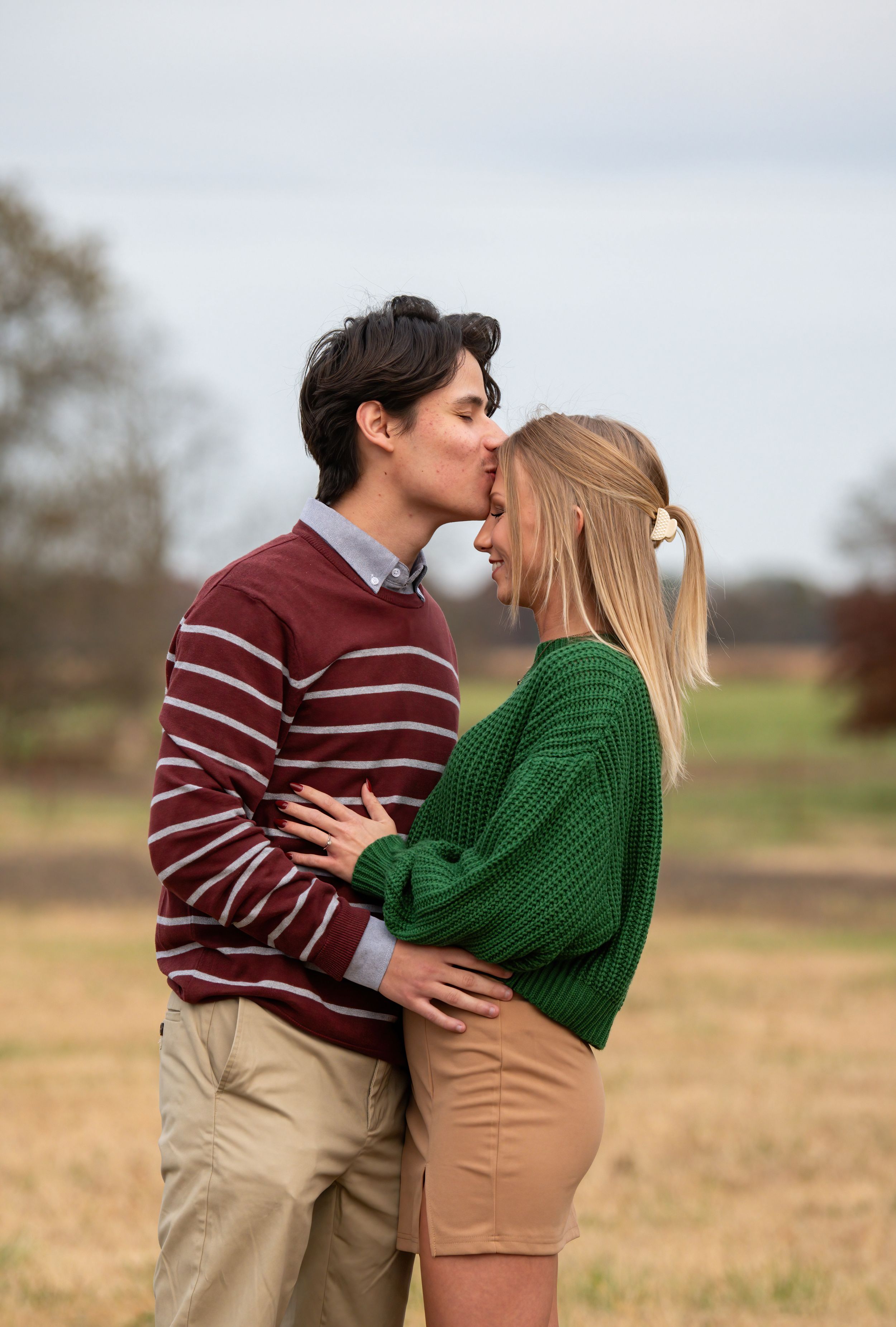 A couple in sweaters share an intimate moment in a rural field.
