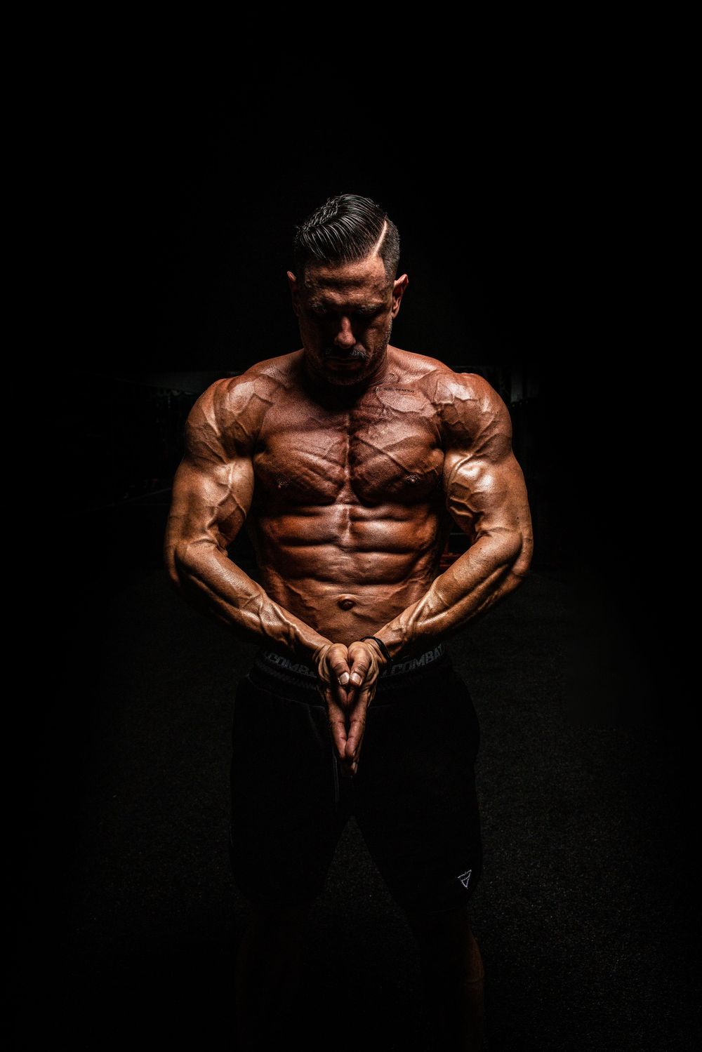 Dramatic studio photos of muscular bodybuilder flexing and posing against dark background to showcase physique.