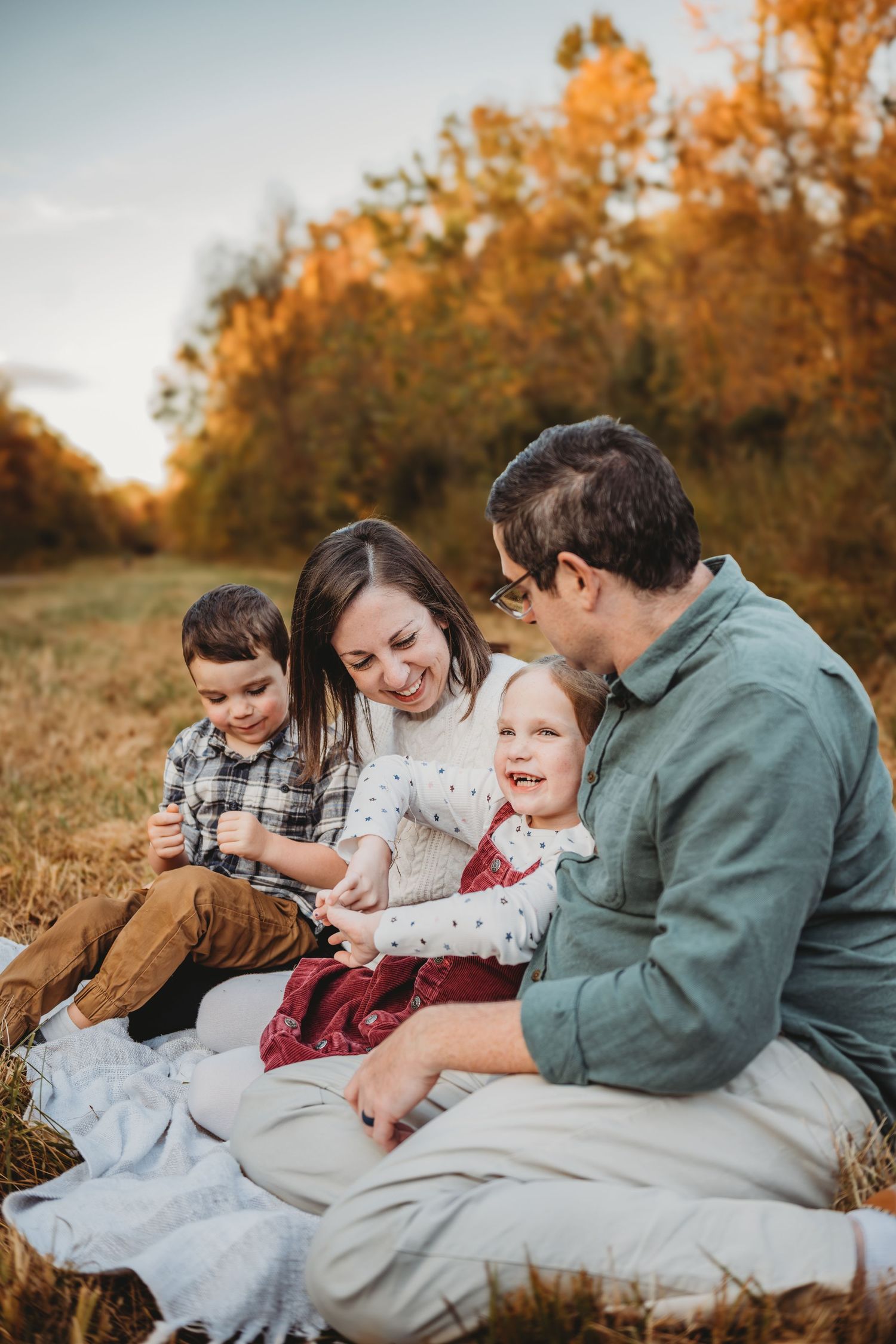 Family portrait at sunset with evergreen trees and golden sunlight filtering through.