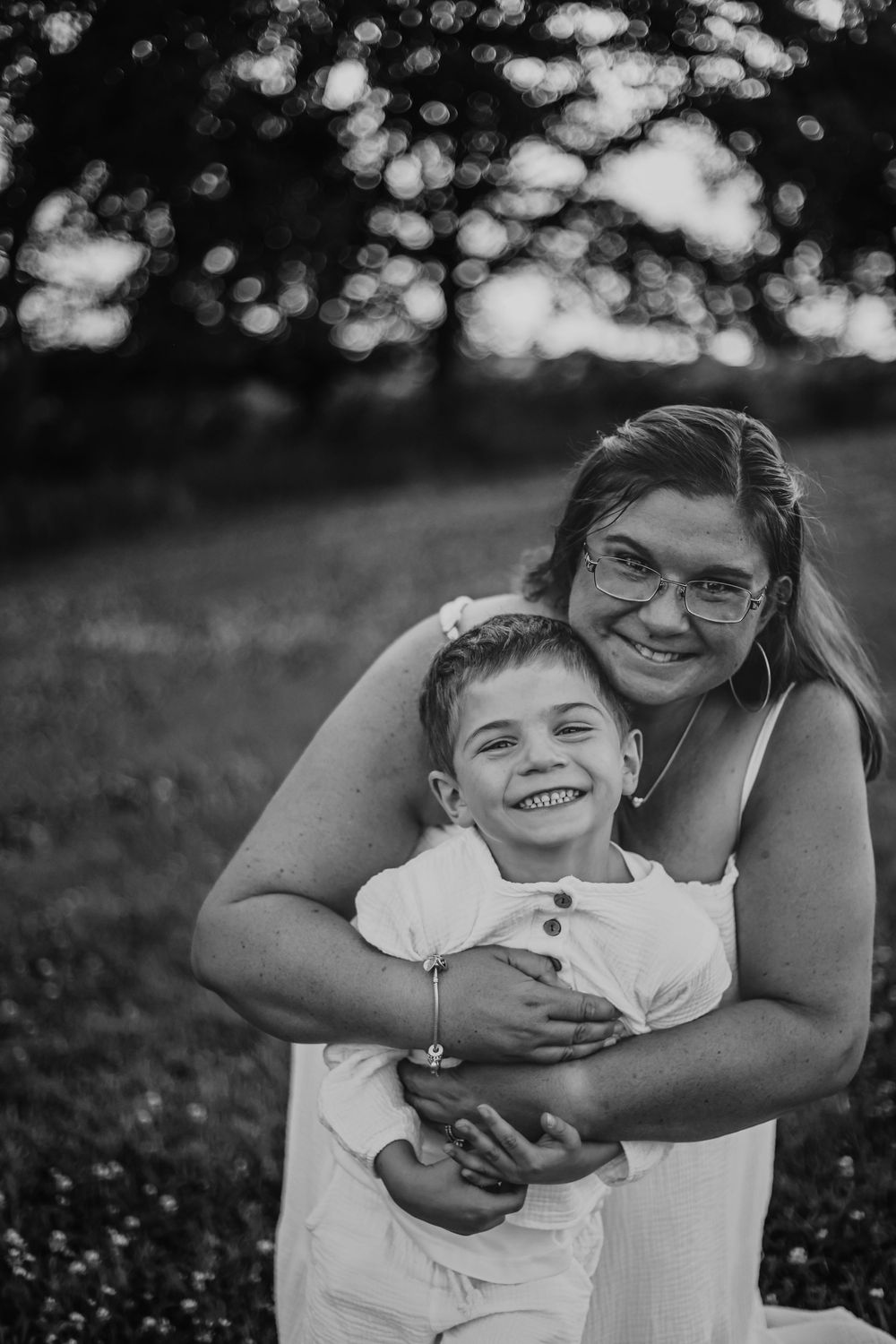 Black and white portrait of two people embracing outdoors with bokeh background. Family photography