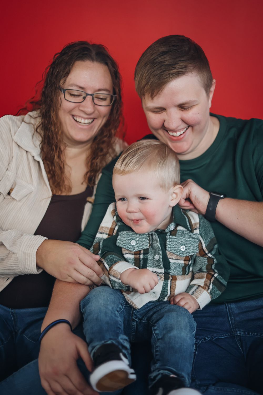 Family sharing joyful moment together on red backdrop while sitting close. Family photography studio